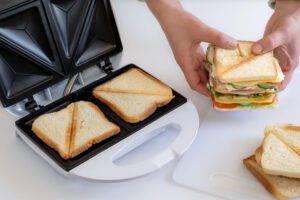 biały opiekacz do kanapek i dłonie trzymające sandwicha